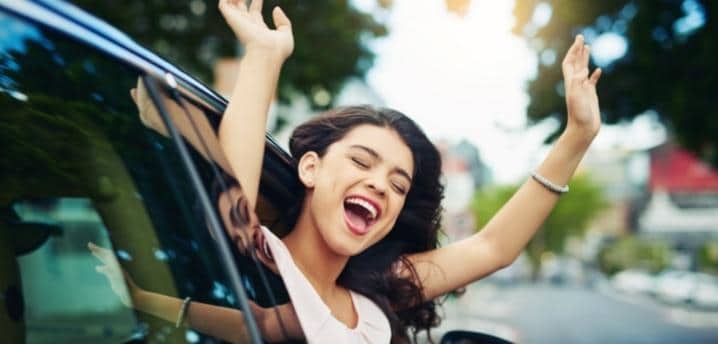 smiling woman leaning out of a car window in her new car